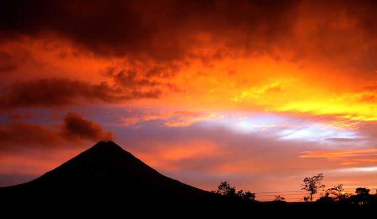 Majestuoso Volcán Arenal en Costa Rica al atardecer, con su cono perfecto elevándose sobre la selva tropical y el cielo anaranjado.